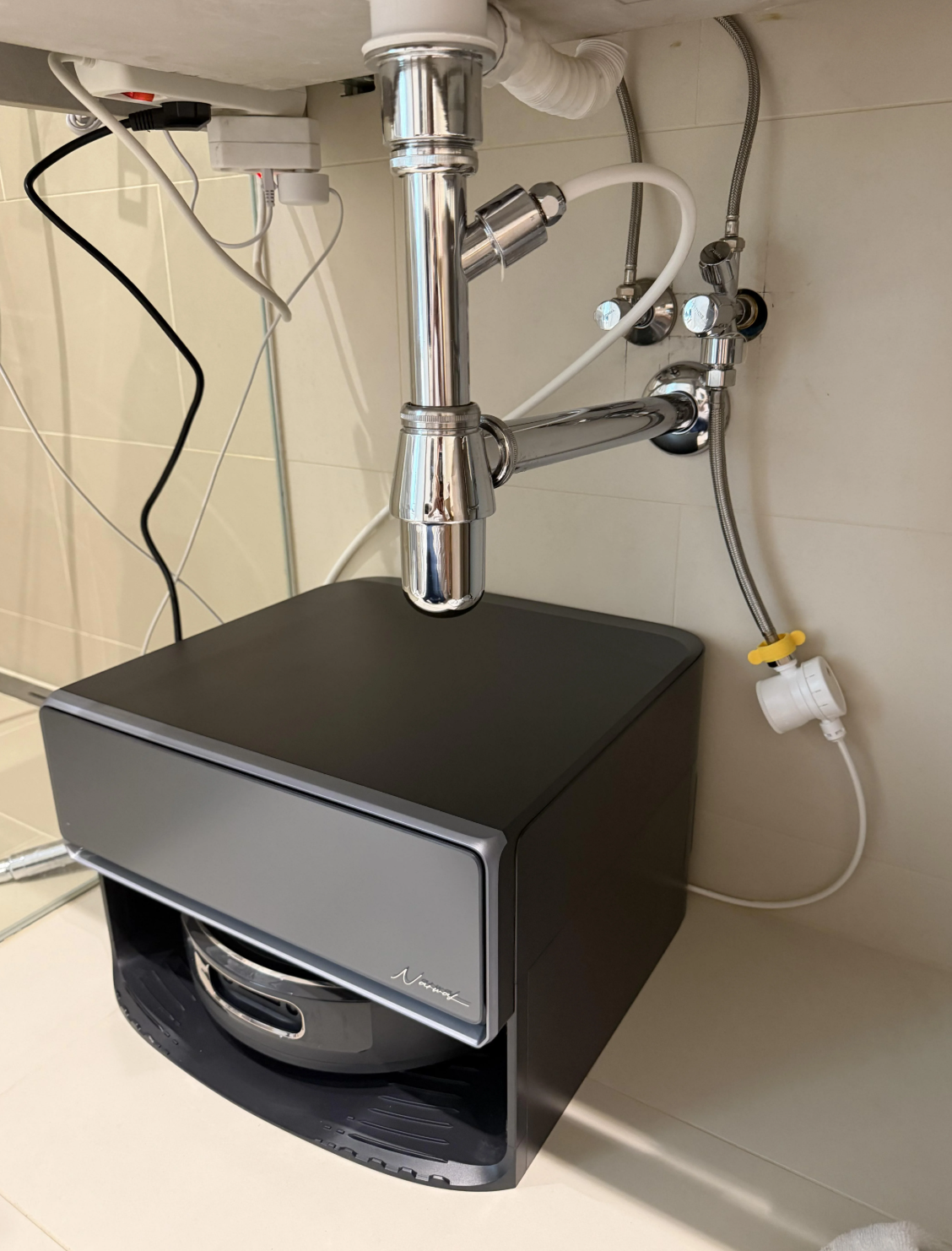The compact automated plumbed base station of the Narwal Flow 2 neatly installed next to a laundry room washing machine line.