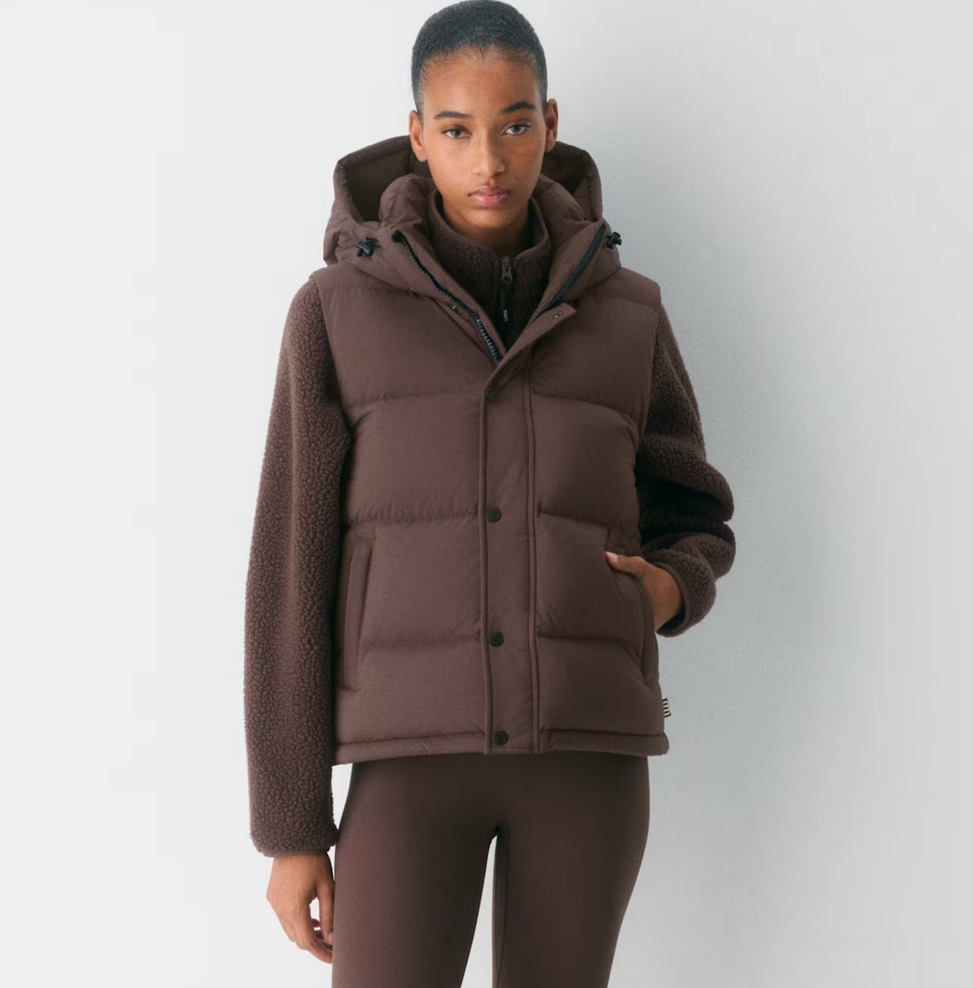Aritzia Super Puff Vest in a neutral color, styled on a model over a sweater.