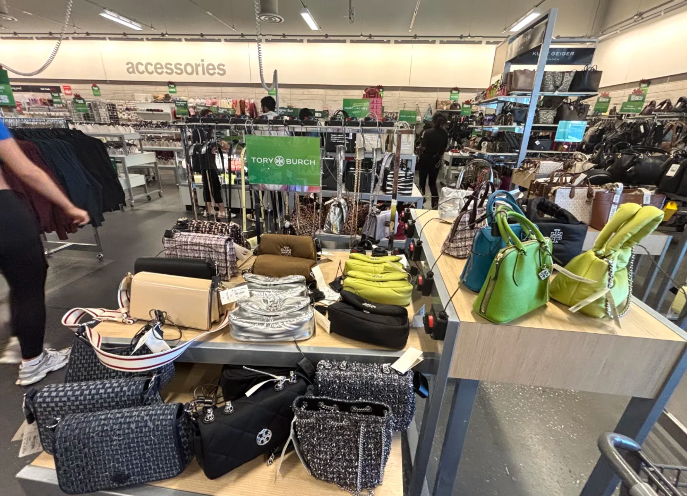 Several Kate Spade handbags in colorful, playful designs, including floral patterns and solid brights, on a retail rack.